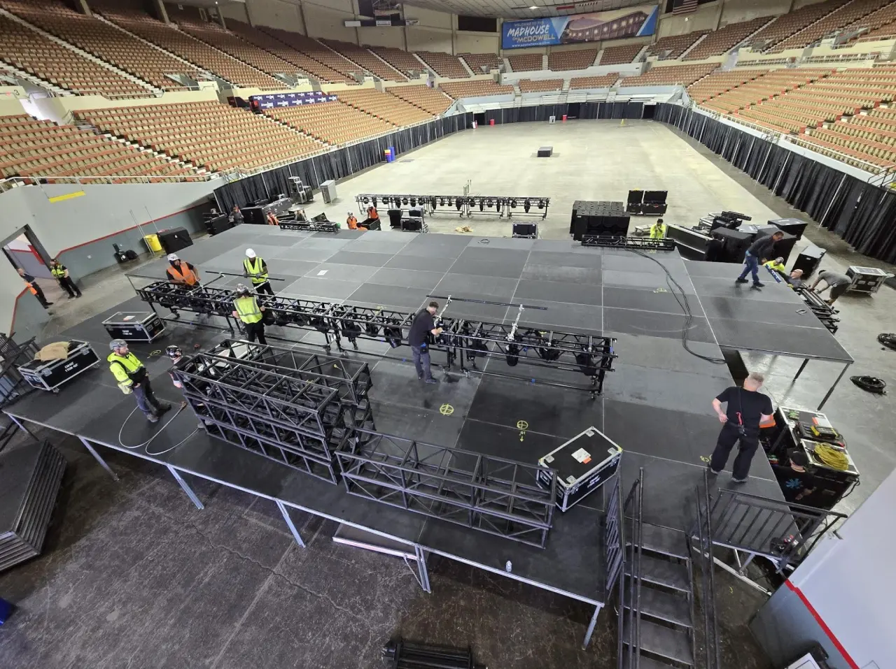 Workers assembling large stage in empty arena.